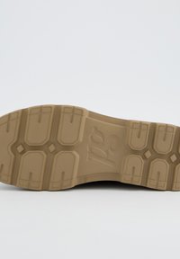 Rubberen schoenloopzool in beige met een gestructureerde oppervlakte. Kenmerkt zich door geperst patroon en een centraal logo. Stevig en ontworpen voor grip.