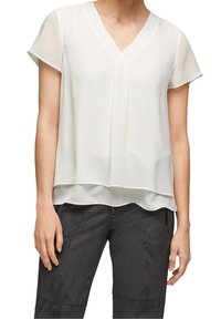 Blusa bianca a maniche corte con scollo a V, dotata di un sottile sovrapposto trasparente e pieghe sottili. L'orlo inferiore è leggermente più lungo, drappeggiando delicatamente.