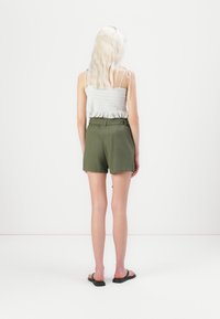 Shorts verts taille haute avec une taille ceinturée, fabriqués en tissu léger. Associés à un haut léger à dos à bretelles texturé.