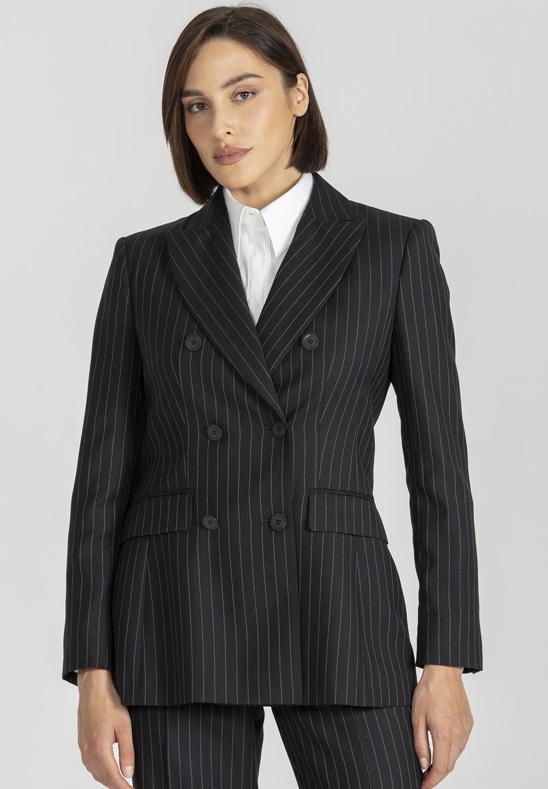 Czarna marynarka w paski, dwurzędowa, z dwoma przednimi kieszeniami i guzikami, o dopasowanym kroju, połączona z białą koszulą.