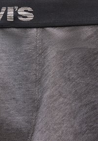 Gros plan sur un tissu gris texturé avec une ceinture noire présentant un texte blanc partiel "vi's" sur le bord supérieur.