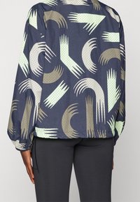 Kurtka wiatrówka w kolorze granatowym z abstrakcyjnymi wzorami w kolorze mięty i beżu, z fakturowanym wykończeniem, elastycznymi mankietami i ściągaczem u dołu.