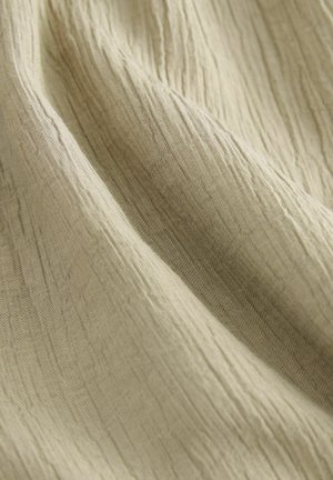 Tessuto di un beige chiaro, stropicciato, con una superficie testurizzata, che mostra sottili linee verticali e una finitura morbida e leggermente lucida.