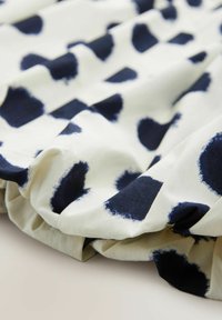 Tessuto di cotone con un fondo bianco e grandi pois astratti blu marino, con una texture arricciata lungo i bordi.
