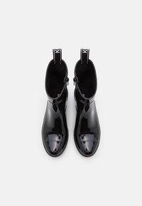 Bottines chelsea noires en vernis avec une finition lisse et brillante, bout rond, panneaux élastiques sur les côtés et languettes à l'arrière pour un enfilage facile.