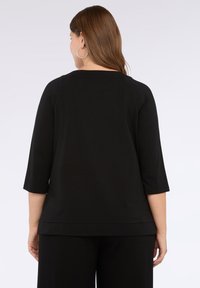 Top nero a maniche 3/4 con scollatura rotonda e vestibilità comoda. Realizzato in materiale morbido, presenta un orlo dritto e dettagli minimi.