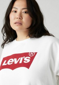 T-shirt bianco in cotone con un grande logo rosso di Levi's. Tessuto liscio, scollatura rotonda e maniche corte. Focalizzato sui dettagli del design frontale.