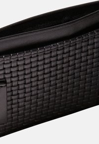 Czarna pleciona skórzana kopertówka o fakturowanej powierzchni i gładkiej wyściółce wewnętrznej. Charakteryzuje się minimalistycznym designem i brakiem widocznych elementów metalowych.