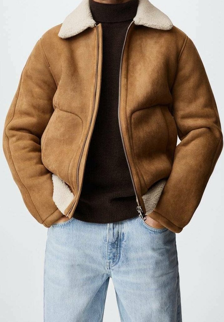 Brun ruskindsjakke med en cremefarvet lammeskinds-krave, lynlåslukning og tekstureret stof. Kombineret med en mørk sweater og lyse denimjeans.