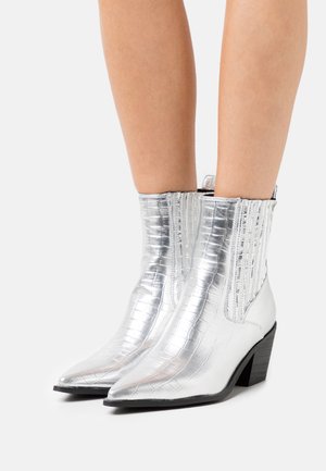 Bottes chelsea argentées avec une texture crocodile brillante, un bout pointu, des panneaux latéraux élastiques et un petit talon carré.