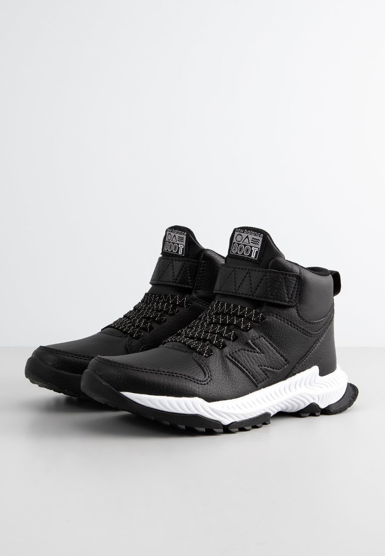 Bottes de sport noires avec une tige en cuir texturé, des lacets élastiques et une sangle Velcro. Dotées d'une semelle intermédiaire blanche et d'une semelle extérieure en caoutchouc.