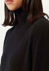 Svart polotröja med ribbad krage, som har ett mjukt, texturerat material och en ledig passform, med sömlös konstruktion.