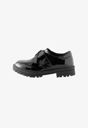 Chaussure en cuir verni noir avec une épaisse semelle en caoutchouc et une fermeture lacet large en ruban sur fond blanc.