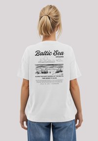 Weißes Baumwoll-T-Shirt mit einem grafischen Druck auf der Rückseite, der die Ostsee darstellt, mit Text und Linienstilelementen. Lockere Passform.
