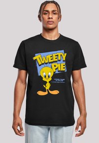 Čierne tričko s jasne žltým kresleným vtákom Tweety, veľkými očami a oranžovými nohami. Text v žiarivých žltých a modrých farbách.