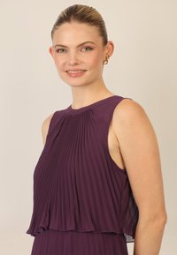 Violetti pliseerattu paita kerroksellisella muotoilulla, jossa on pyöreä pääntie ja hihaton tyyli. Silkkinen pinta ja kevyt kangas.