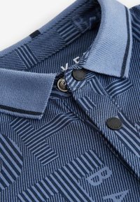 Navy polo shirt with a textured pattern featuring stripes and geometric shapes. Blue collar with two black buttons and subtle branding inside.