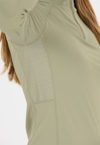 Close-up of a person in a light green long-sleeve top with mesh ventilation panels under the arm and along the side.