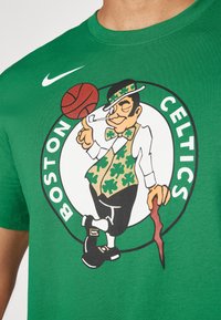 Πράσινο βαμβακερό T-shirt με λογότυπο των Boston Celtics που απεικονίζει έναν λεφτά=η που κρατάει μπάσκετ, περιτριγυρισμένο από το κείμενο "BOSTON CELTICS."