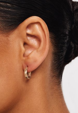 Gold hoop earring with a twisted design, featuring a textured surface. The earring hangs from a small clasp near the ear.