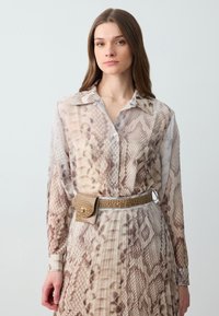 Sheer shirt with a snake pattern in earthy tones, featuring a collar and button closure, paired with a textured gold belt with a clasp.