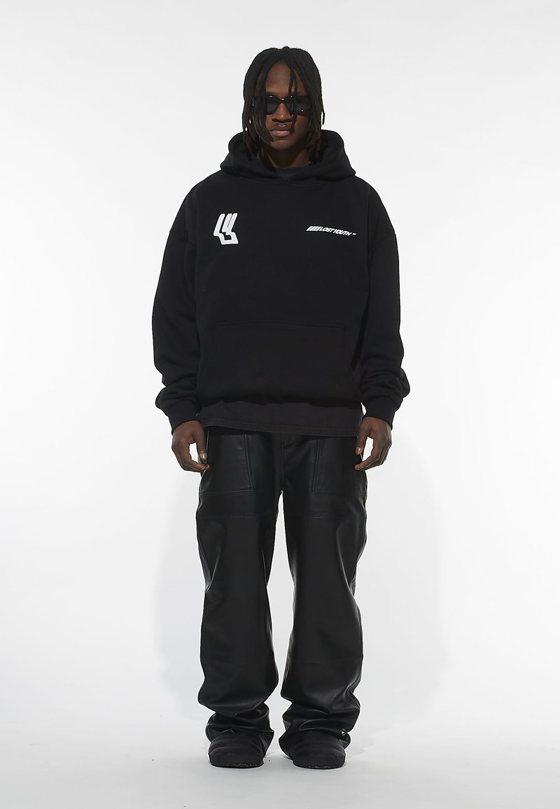 Sort bomulds hoodie med forlommer og hvidt logo. Parret med løse sorte læderbukser. Modellen bærer solbriller. Minimalistisk design.