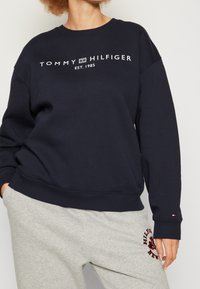 Felpa blu navy in cotone con polsini e orlo a coste, con il logo bianco "TOMMY HILFIGER EST. 1985" sulla parte anteriore.