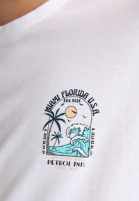 Hvid bomulds T-shirt med et grafisk print af palmer, bølger og en sol, med teksten "Miami Florida U.S.A." og "Petrol Ind."