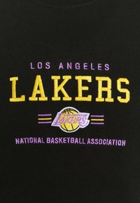 Tissu noir avec texte brodé en jaune et violet : "LOS ANGELES LAKERS" et logo avec un ballon de basket, ainsi que "NATIONAL BASKETBALL ASSOCIATION."