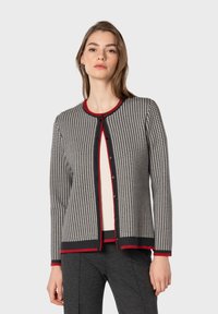 Cardigan lavorato a maglia in pattern houndstooth nero e crema, con bordi ribattuti rossi e bottoni neri. Presenta un collo rotondo e maniche lunghe.