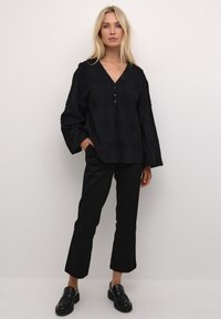 Blusa nera con scollo a V, apertura con bottoni e motivo floreale testurizzato. Abbinata a pantaloni dritti neri e mocassini neri.