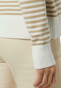 Gestreifter Pullover in Beige- und Weißtönen, mit gerippten Bündchen und weichem Strickmaterial, kombiniert mit cremefarbenen, eng anliegenden Hosen.