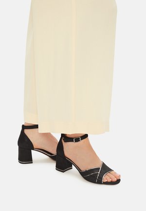 Schwarze, offene Sandalen mit Absatz, strukturiertem Obermaterial, Knöchelriemen und Blockabsatz. Silberne Akzente am Zehenbereich und eine glatte Sohle.