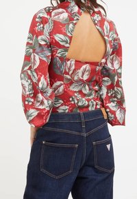 Rode bloemenblouse met pofmouwen en een keyhole rug, gecombineerd met donkerblauwe jeans met contrasterende stiksels en twee achterzakken.