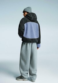 Fleece hoodie met grijze en blauwe panels, gecombineerd met losse grijze sweatpants en een lichtgrijze beanie. Heeft een casual ontwerp met textuurstof.