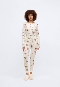 Long-sleeve, floral-print pajama set in cream with a fitted design, elastic waistband, and matching slippers with a soft texture.