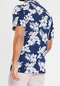 Laivastonsininen lyhythihainen paita, jossa valkoisia kukkakuoseja ja lehtiä. Kauluksellinen malli, rento istuvuus ja sileä kangaspinta.