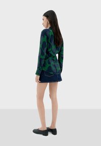 Camisa de manga larga con patrón abstracto verde y azul marino, combinada con una falda mini de mezclilla y zapatos planos negros. Tela suave, corte relajado.