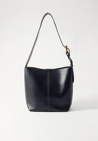 Zwarte leren totebag met een gladde textuur, een enkele schouderriem en contrasterend bruine stiksels langs het voorpaneel.