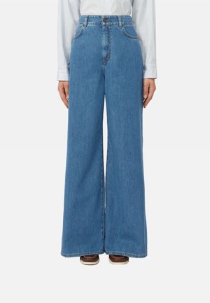 Jeans blu a vita alta e gamba larga indossati con una camicia a righe infilata e scarpe marroni visibili all'orlo.