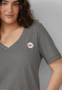 Gestreiftes Schwarz-Weiß V-Ausschnitt-Shirt mit kurzen Ärmeln, das ein pinkes, rundes "JOY."-Grafikdesign auf der Brust hat. Weicher Stoff.