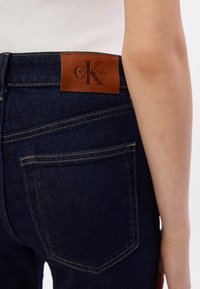 Granatowe dżinsy wykonane z denimu z skórzaną naszywką z logo Calvin Klein w talii, z standardowymi tylnymi kieszeniami oraz detalami w kontrastowym ściegie.
