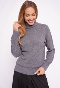 Szary dziergany sweter z wysokim golfem, ściągaczami na rękawach i u dołu; miękka faktura o lekko luźnym kroju. Noszony z czarnymi plisowanymi spodniami.