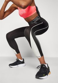 Leggings bianco e nero a vestibilità slim, con pannelli laterali bianchi e una vita PUMA. Abbinati a scarpe da atletica nere.
