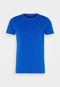 Blå bomullströja med rundad halsringning, korta ärmar och en liten broderad logotyp på bröstet. Slät textur, avslappnad passform.