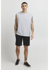 Gray sleeveless t-shirt, black shorts, and black sneakers; casual fit; smooth texture; model with visible tattoos standing on a plain background.