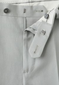 Lysegrå bukseelastik med en metal krogspænde, knap og synlige knaphuller, der viser lukningsdetaljer.