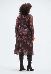 Rochie lungă neagră transparentă cu model floral roz, cu mâneci lungi și siluetă fluidă, asortată cu cizme negre cu toc până la genunchi.