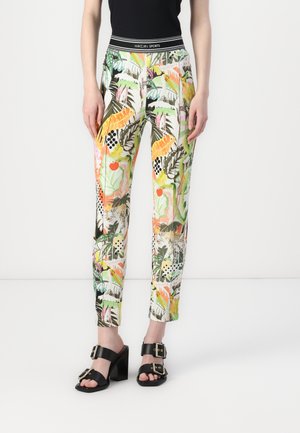 Colorful printed trousers featuring tropical patterns with greens, yellows, and pinks; solid black waistband with logo accents; paired with black heeled sandals.