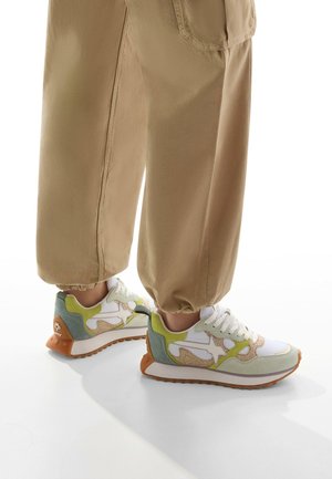 Multicolored sneaker with a white mesh upper, green and beige suede accents, and a textured orange rubber sole. Elastic ankle cuffs on pants.